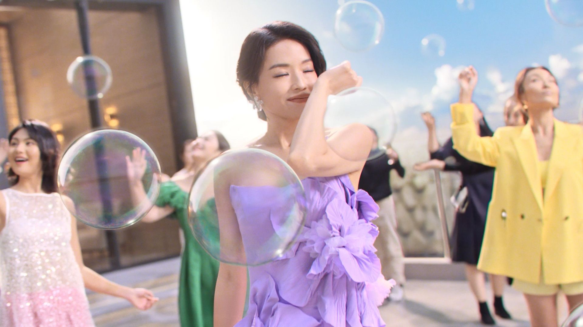 身穿色彩鮮豔的洋裝和套裝的女性們置身於戶外巨大的半透明泡泡之中。
